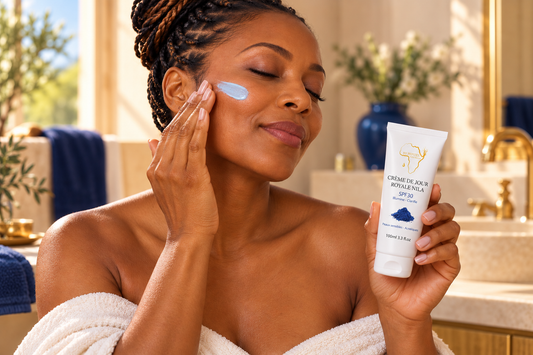Femme à la peau métissée appliquant la Crème Jour SPF30 Correctrice au Nila sur sa joue dans une lumière matinale